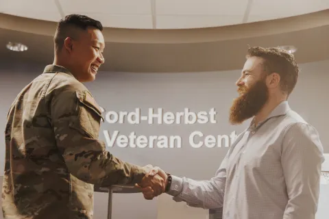  military student shaking hands with staff member in front of the Veteran Center sign